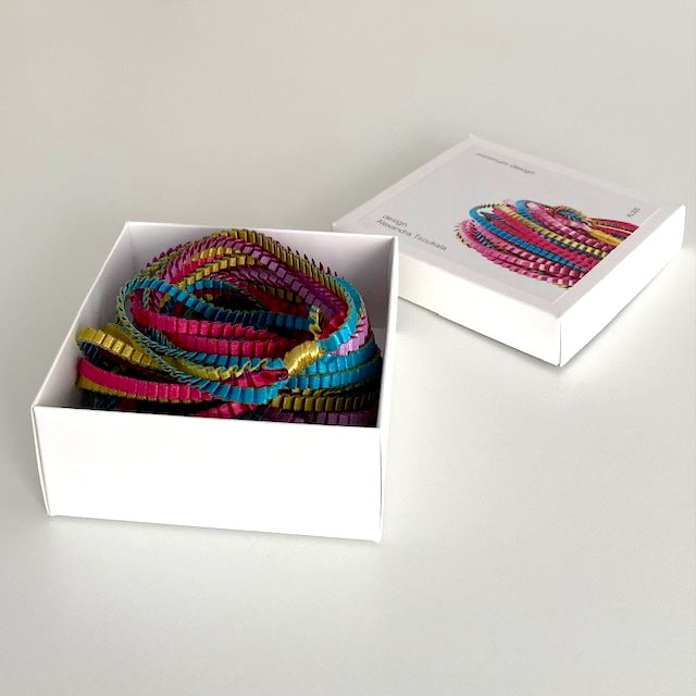 Long sautoir composé de huit bandes de trois millimètres de satin plissé de couleur, doré, turquoise, fuchsia, lilas,reliées les unes aux autres par un lien de coton jaune d'or. Bijou présenté dans sa boîte en carton blanc.
