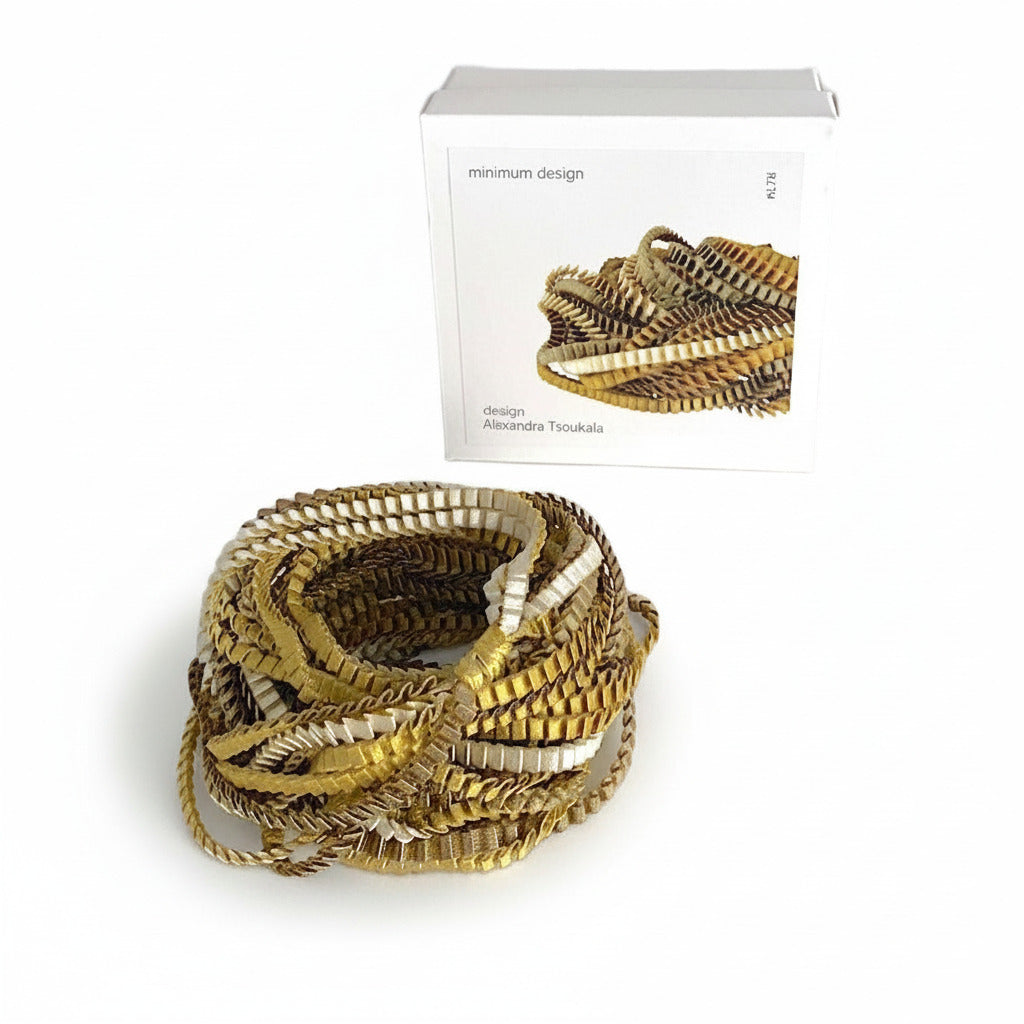 Long sautoir de couleur kaki, ivoire et doré composé de huit bandes de trois millimètres de satin plissé reliées les unes aux autres par un lien de coton jaune d'or. Bijou présenté dans sa boîte en carton blanc.