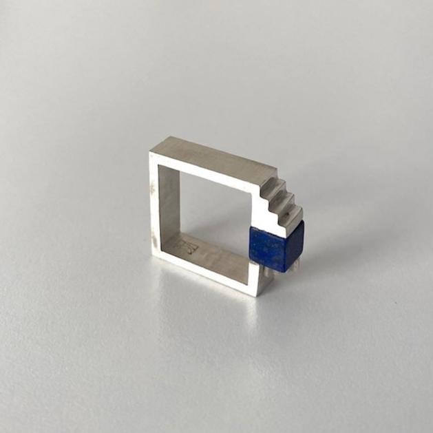 Bague carrée en argent brossé, au centre un cube de lapis-lazuli est serti entre deux éléments inversés en forme d'escalier.