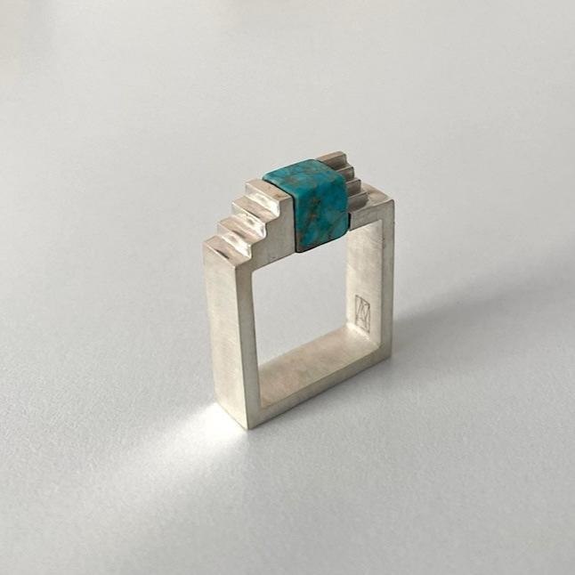 Bague carrée en argent brossé, au centre turquoise taillée en cube est enchâssée entre deux éléments inversés en forme d'escalier.