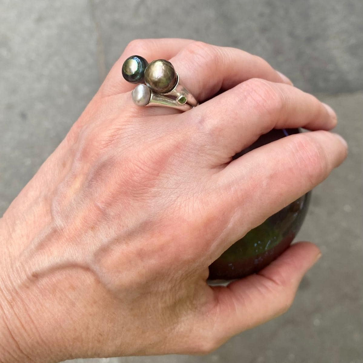 Bague ouverte présentant trois perles de Tahiti de couleurs différentes. Son anneau en argent sculpté est orné de petites pierres de couleurs.