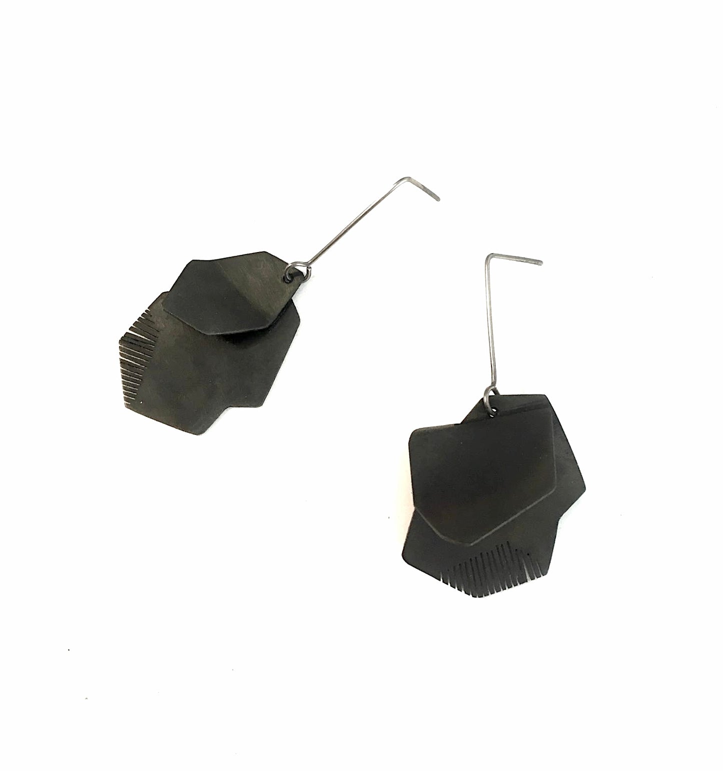 Boucles pendantes architecturales en acier patiné noir, plié et scié par endroit en lamelles. Elles sont montées sur des tiges droites en titane.