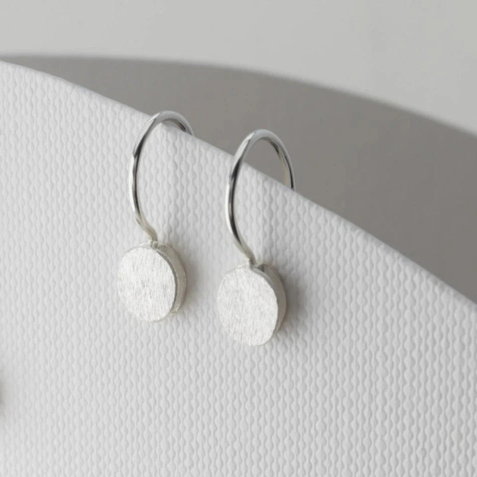 Petites boucles d'oreilles pendantes composées de deux éléments ronds superposés en forme de galet en argent brossé. Fermoirs crochets.