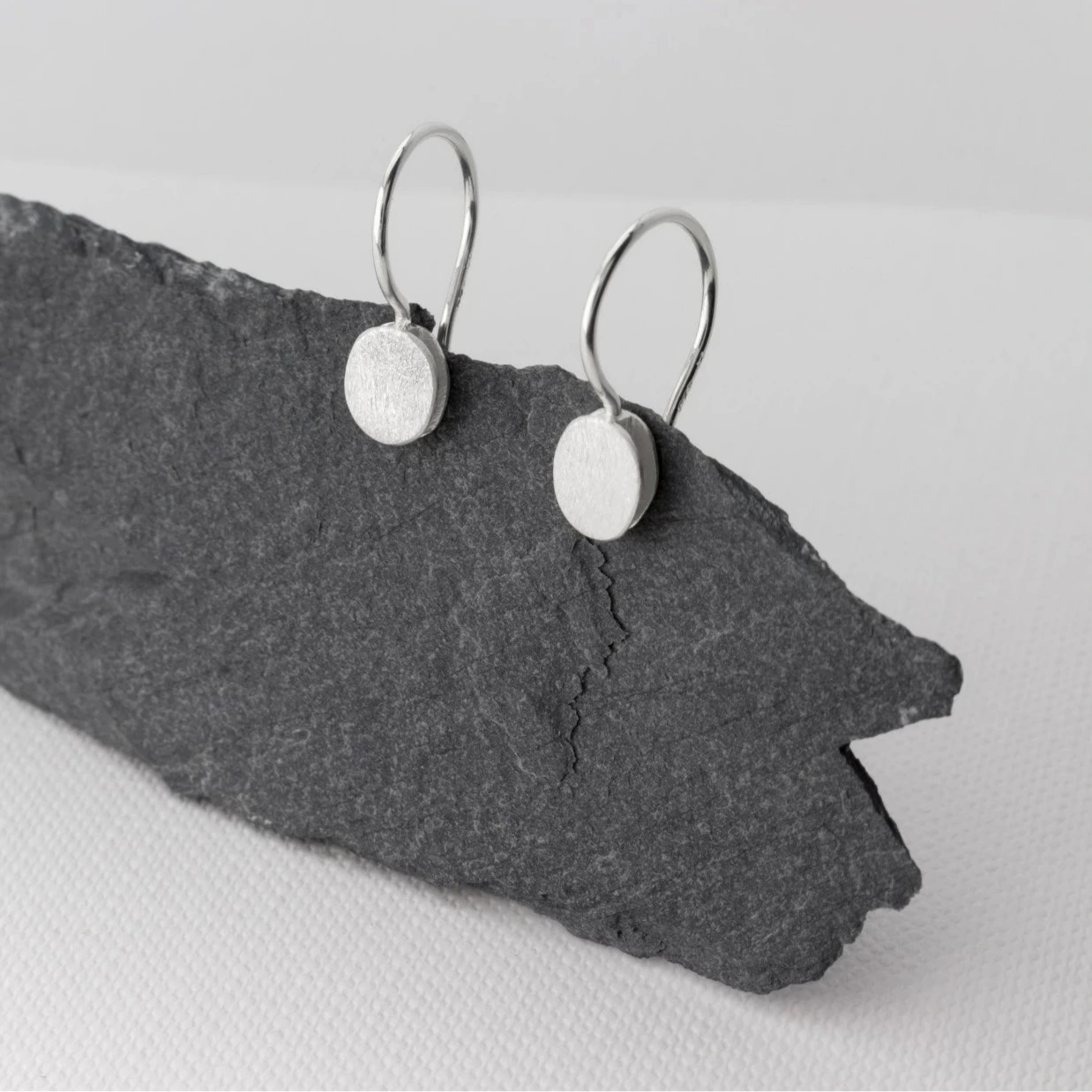 Petites boucles d'oreilles pendantes composées de deux éléments ronds superposés en forme de galet en argent brossé. Fermoirs crochets.