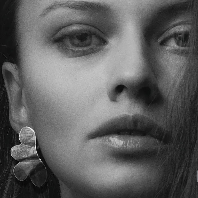 Boucles d'oreilles sculptées en bronze laminé et peintes à la main, elles présentent une forme de demi-fleur minimaliste. Boucles portées.