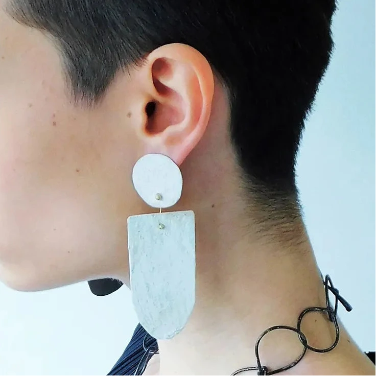 Boucles pendantes aux formes géométriques sont réalisées en bronze peint à la main avec des pigments acryliques. Elles sont légères et confortables à porter au quotidien. Création artisanale de l'artiste grecque Dora Haralambaki. Boucle portée, vue de profil.