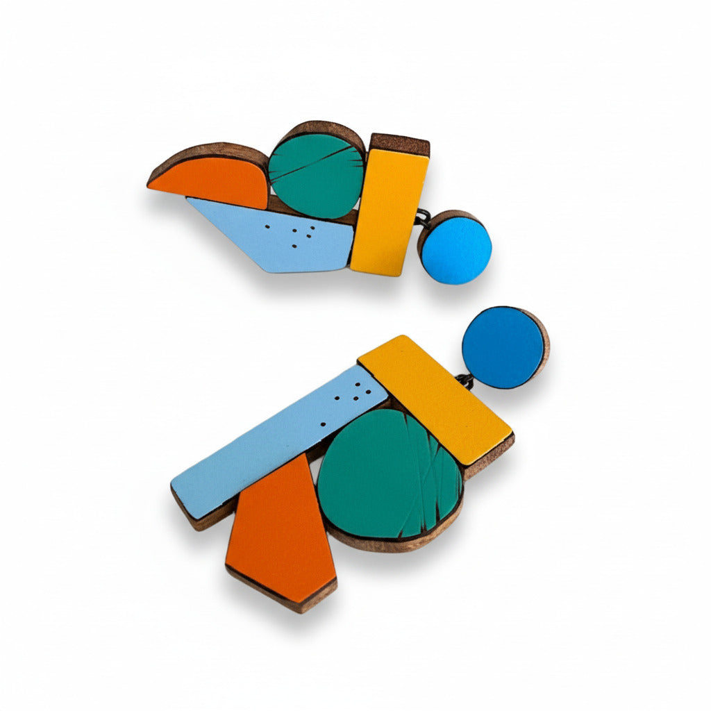 Suspendues à un support rond bleu, ces boucles XL mêlent bois et formica mat ou brillant, rayé ou ponctué de petits points noirs. Leur design épuré met en valeur des éléments assemblés entre eux de couleurs franches – jaune, vert, orange et bleu. Création Karen Vanmol, artiste belge.