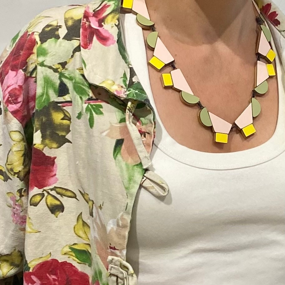 Ce collier design réunit 12 éléments géométriques en bois et formica rose poudré, vert, pastel et jaune clair reliés par des attaches en argent patiné noir et fermés par un fermoir crochet. Bijou contemporain fait à la main par l'artiste belge Karen Vanmol. Joyeux et moderne, il s'adapte à toutes les encolures.