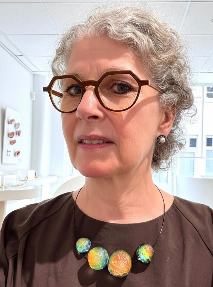 Ce collier Météorites se compose de 4 sphères en résine texturée assemblées sur un câble noir. L'effet irisé et changeant s'inspire des teintes naturelle, des opales. Détail du bijou porté.