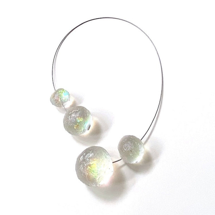 Le collier Météorites se compose de quatre sphères en résine transparente texturée, assemblées sur un câble gris. Le fermoir aimanté, intégré dans deux éléments de résine, assure une finition harmonieuse et pratique.