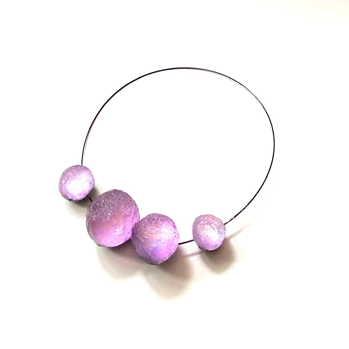Tour de cou composé de 4 sphères en résine texturée couleur Lilas assemblées sur un cable noir. Le fermoir est aimanté.