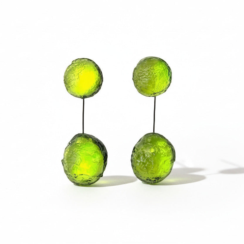 Boucles pendantes vert anis, composées de deux sphères en résine texturée reliées par un câble fin noir et solide. Pour oreilles percées.