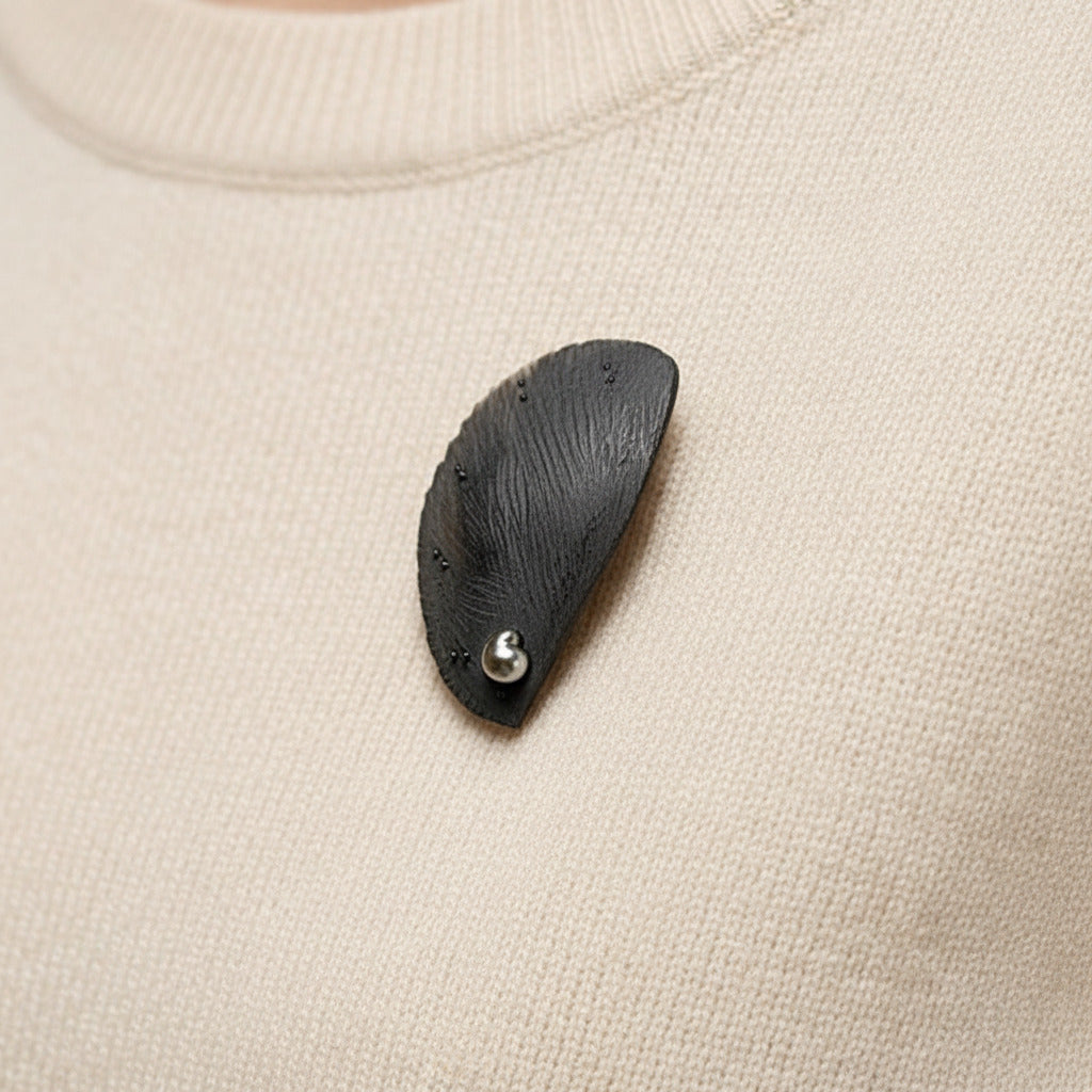 Broche contemporaine en corne brune sculptée et texturée, ornée d'une perle de Tahiti. Bijou en forme de demi cercle porté sur un pull.