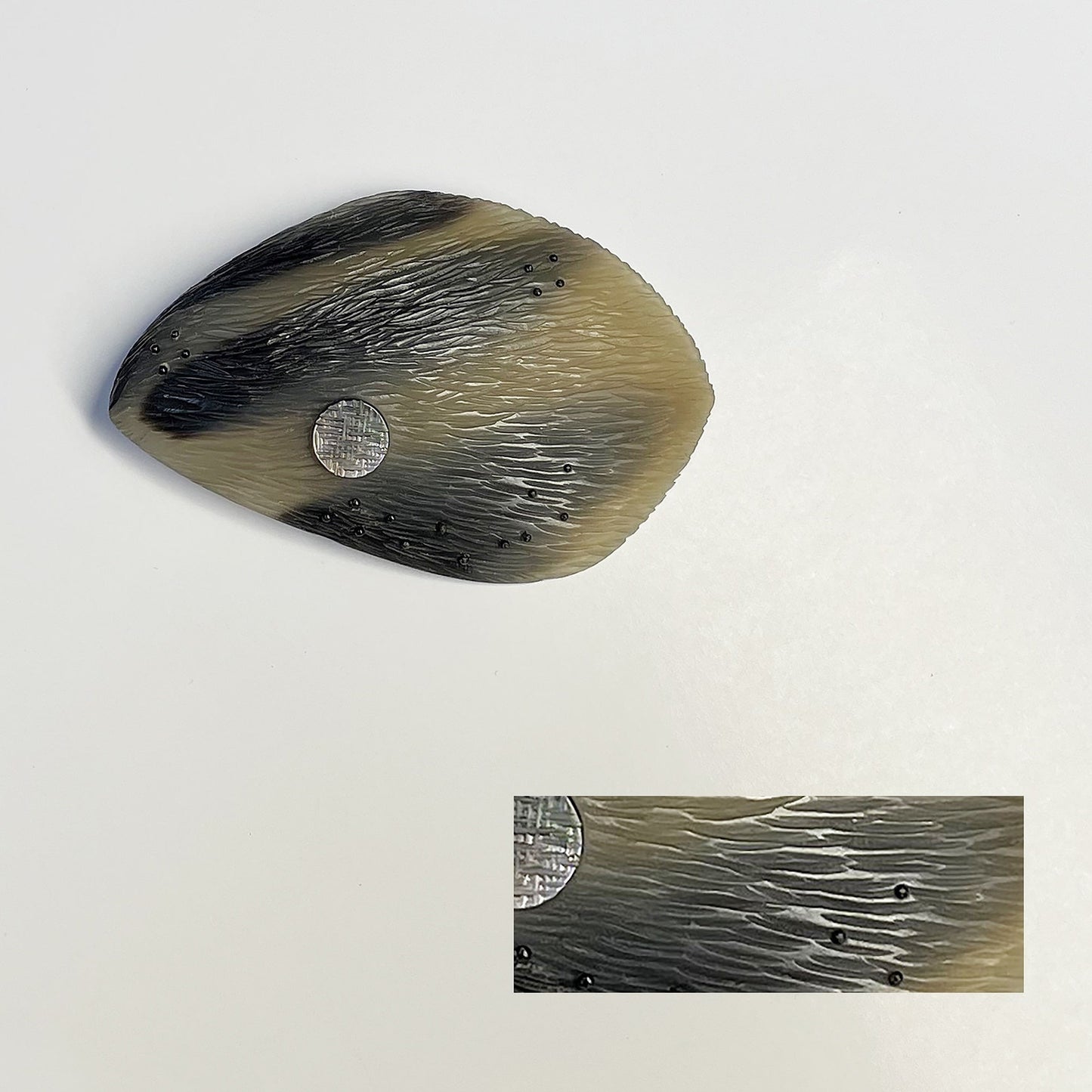 broche ovale, sculptée en corne dorée aux dessins bruns naturels. Le bijou est gravé, orné d'une pastille de nacre grise et de fil de nylon perlé. Une pièce contemporaine réalisée à la main en pièce unique.