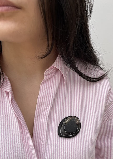 Broche en ébène sculpté et texturé présentant deux ovales dessinés de points blancs et rosés peints à la main. Bijou porté sur chemise.