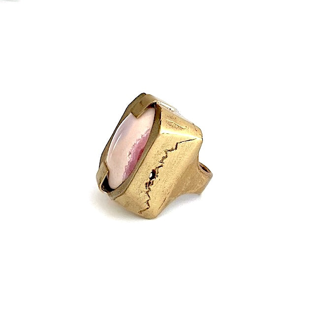 Bague sculpturale rectangulaire en bronze entaillé sur les longueurs. Au centre en cabochon, une Rhodochrosite rose tendre et fuchsia est tenue par deux large griffes.