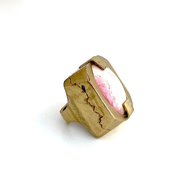 Bague sculpturale rectangulaire en bronze entaillé sur les longueurs. Au centre en cabochon, une Rhodochrosite ovale,rose tendre et fuchsia est tenue par deux large griffes.