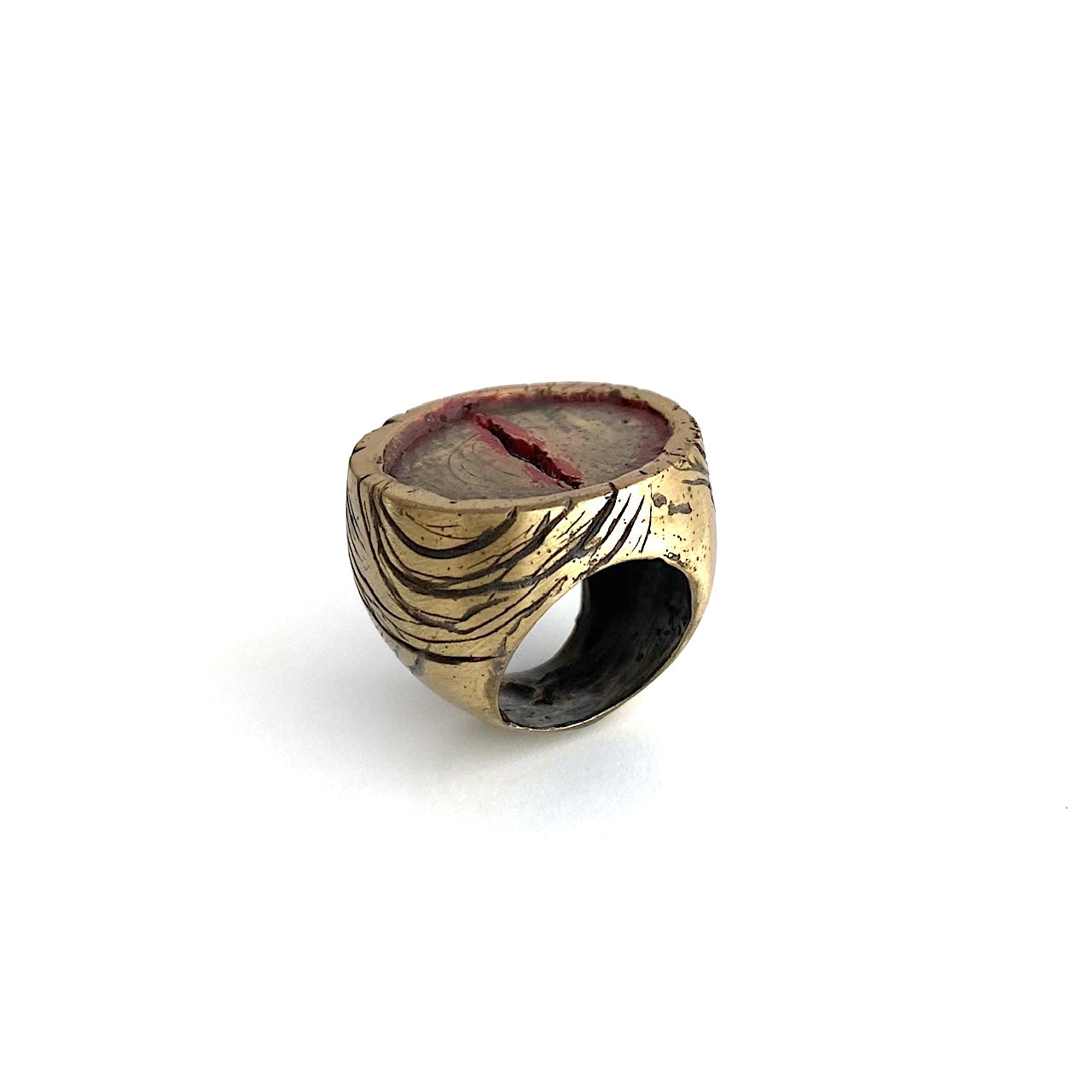 Chevalière sculpturale ronde en bronze , une entaillé au centre dans le métal est soulignée de peinture acrylique rouge. Les flancs la bague sont griffés de noir.