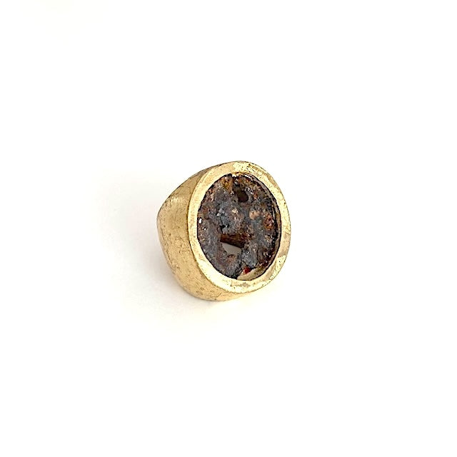 Large chevalière en bronze patiné à la feuille d'or. Une plaque ronde en fer rouillé et usé décore cette bague.