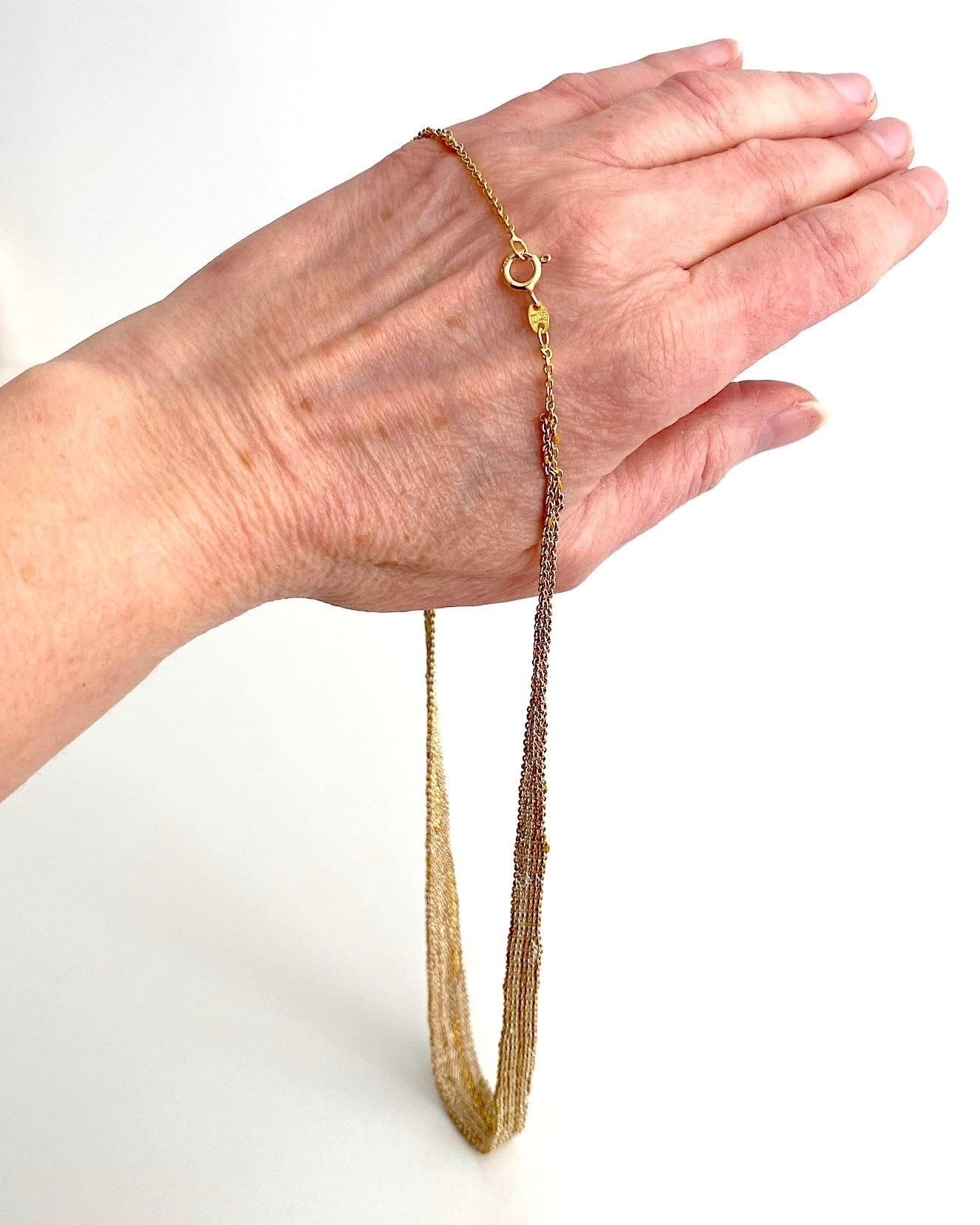 Tour de cou dégradé, forme ruban, composé d'un assemblage de chaînes d'argent dorées au fil de soie. Le collier est présenté suspendu sur une main.