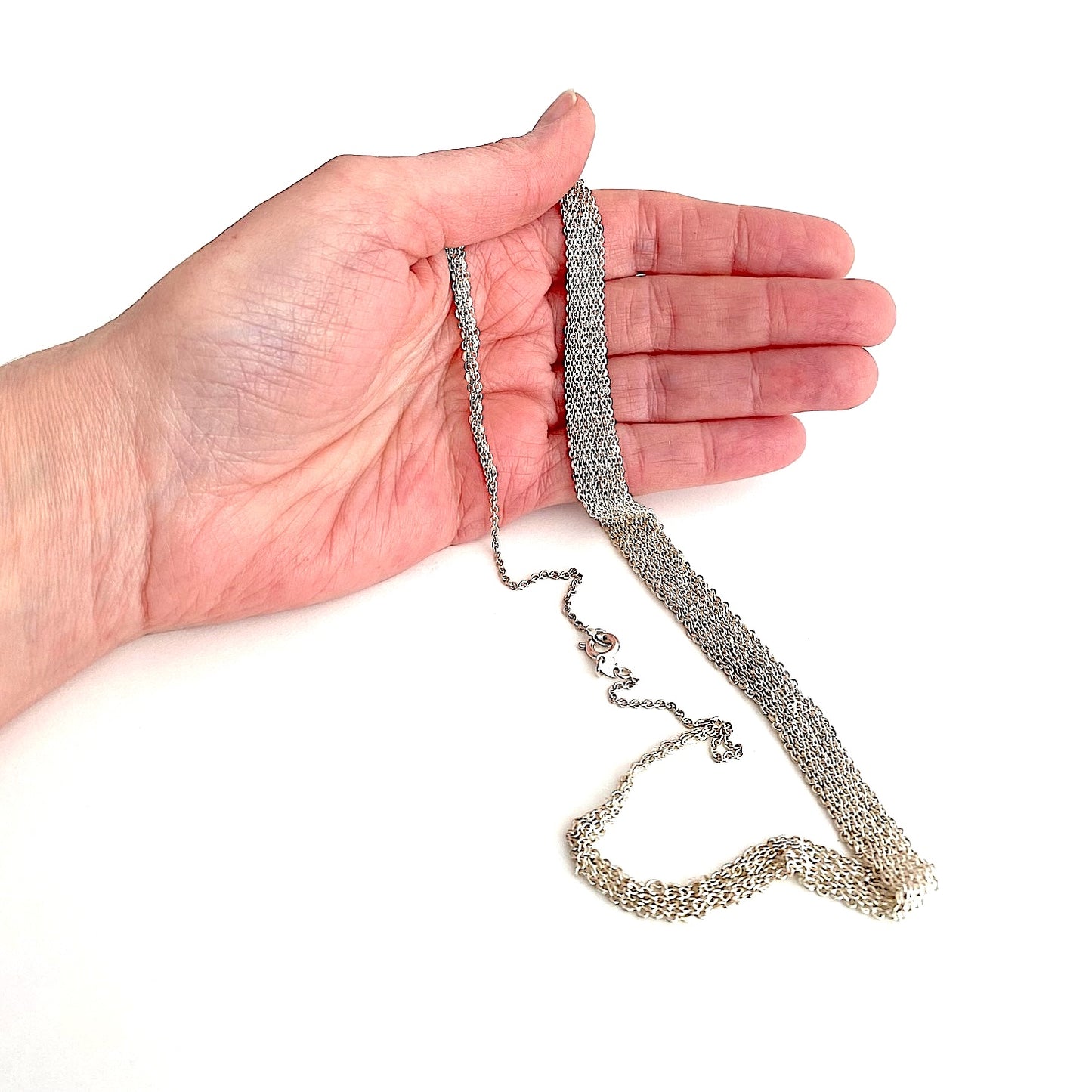 Tour de cou dégradé composé de plusieurs chaînes en argent assemblées les ensemble au fil de soie, présenté sur une main de femme. Fermoir anneau ressort.