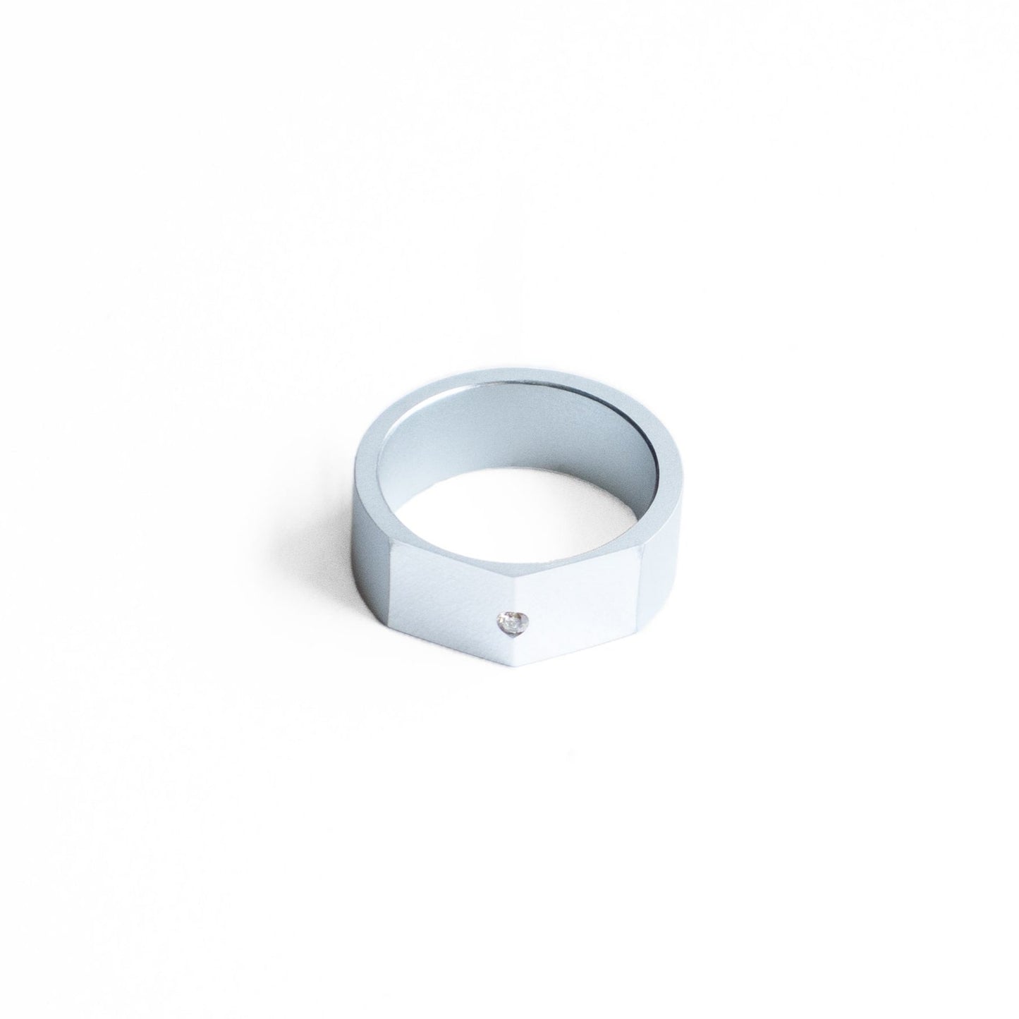 Bague style chevalière, en aluminium anodisé gris.Son design met en valeur le contraste des finition mates et brillantes du métal. Sur le sommet biseauté et poli sur trouve un diamant blanc.
