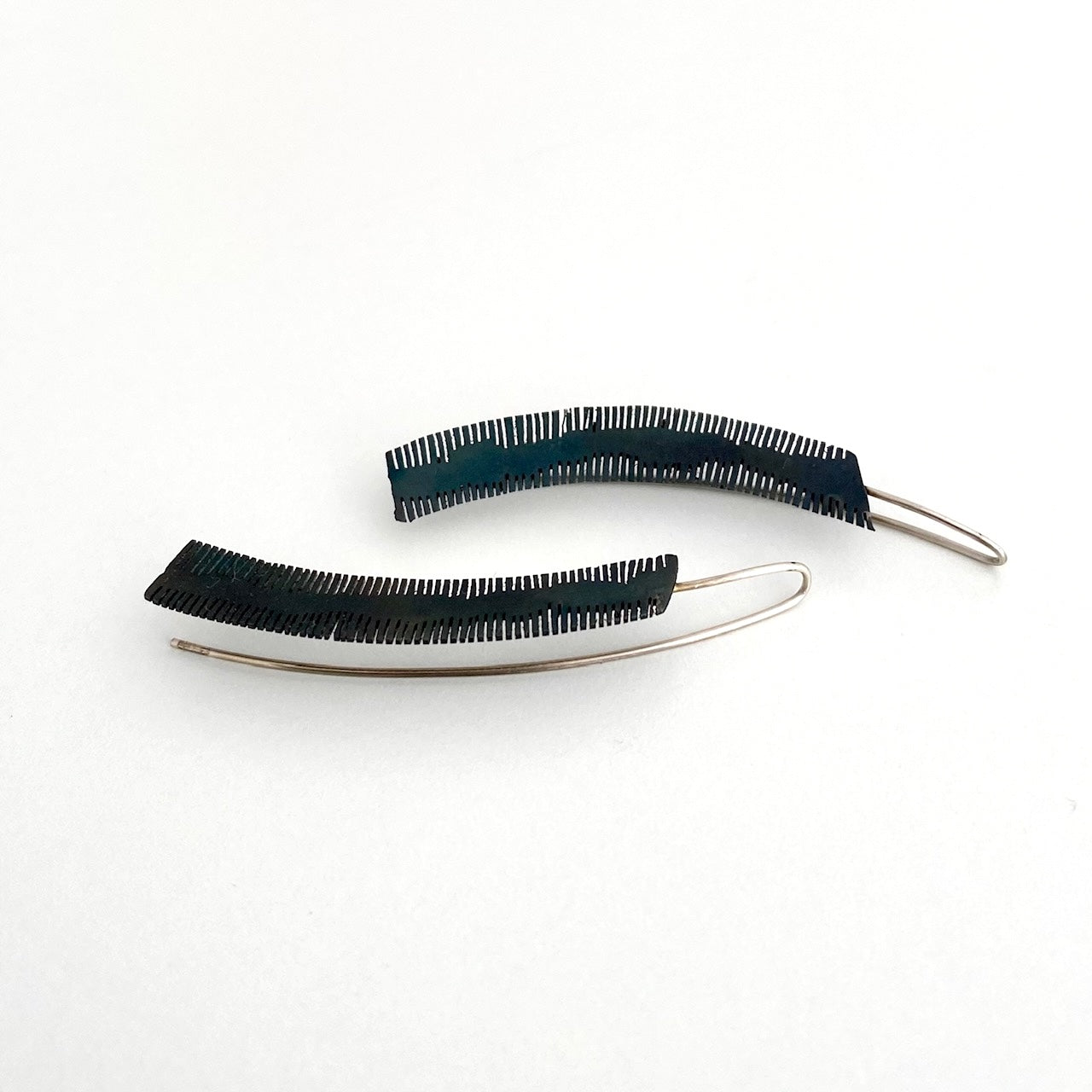 Boucles d'oreilles longues et géométriques découpées dans de l'acier patiné noir. Le métal scié sur la longueur du métal rappelle la délicatesse d'une plume. Une tige d'argent pour fermoir prolonge le bijou.