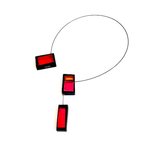 Collier ouvert avec 3 rectangles de résine rouge, orange et rose assemblés sur un câble noir. Fermoir aimant inséré dans la résine. 