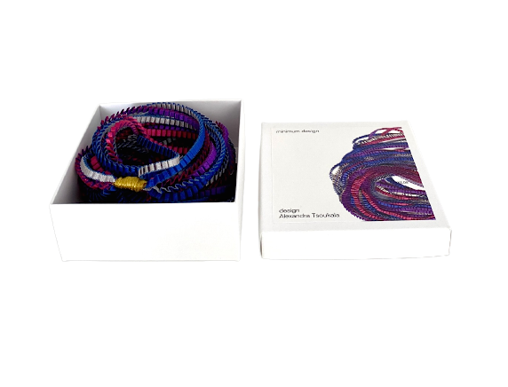 Collier iconique de la créatrice grecque Alexandra Tsoukala présenté dans sa boîte en carton blanc illustrée, prêt à offrir.