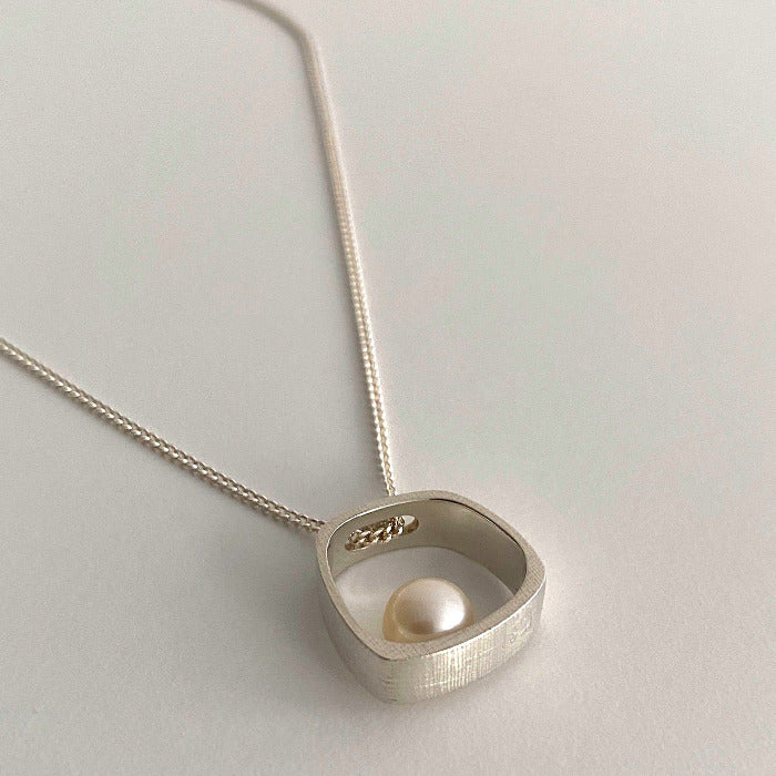 Pendentif argent texturé forme carré orné d'une perle culture blanche, chaîne réglable 45/50cm, posé sur fond blanc