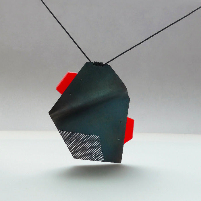 Pendentif sculptural en acier plié et scié avec patine noire et plaque d'acrylique rouge présenté sur lien noir réglable