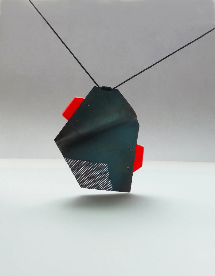 Pendentif acier plié et scié avec patine noire et plaque d'acrylique rouge présenté sur lien noir réglable