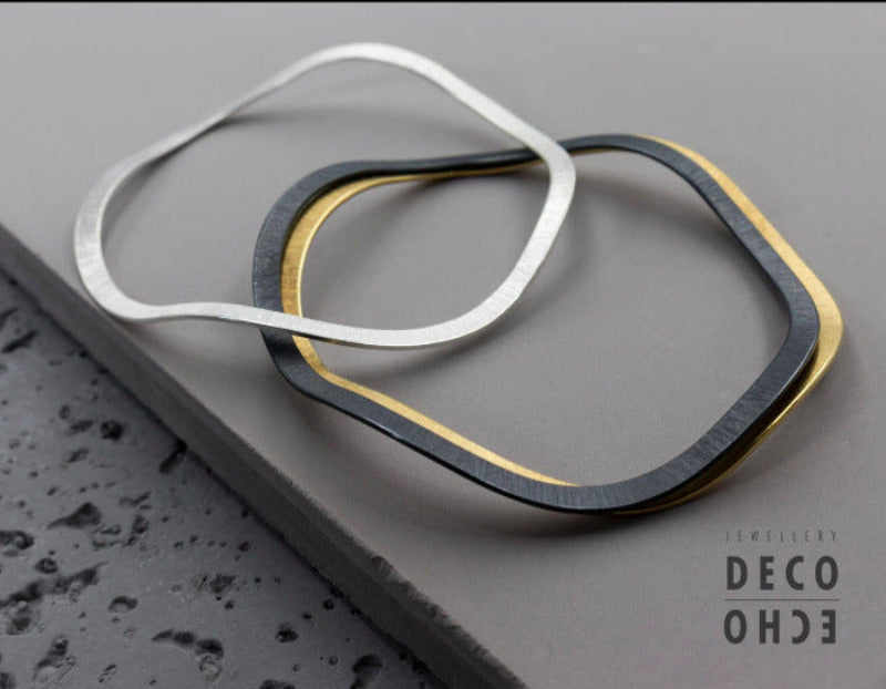 Bracelets fins irreguliers posés sur fond gris,finitions : argent, argent plaqué or jaune 18k,oxydé