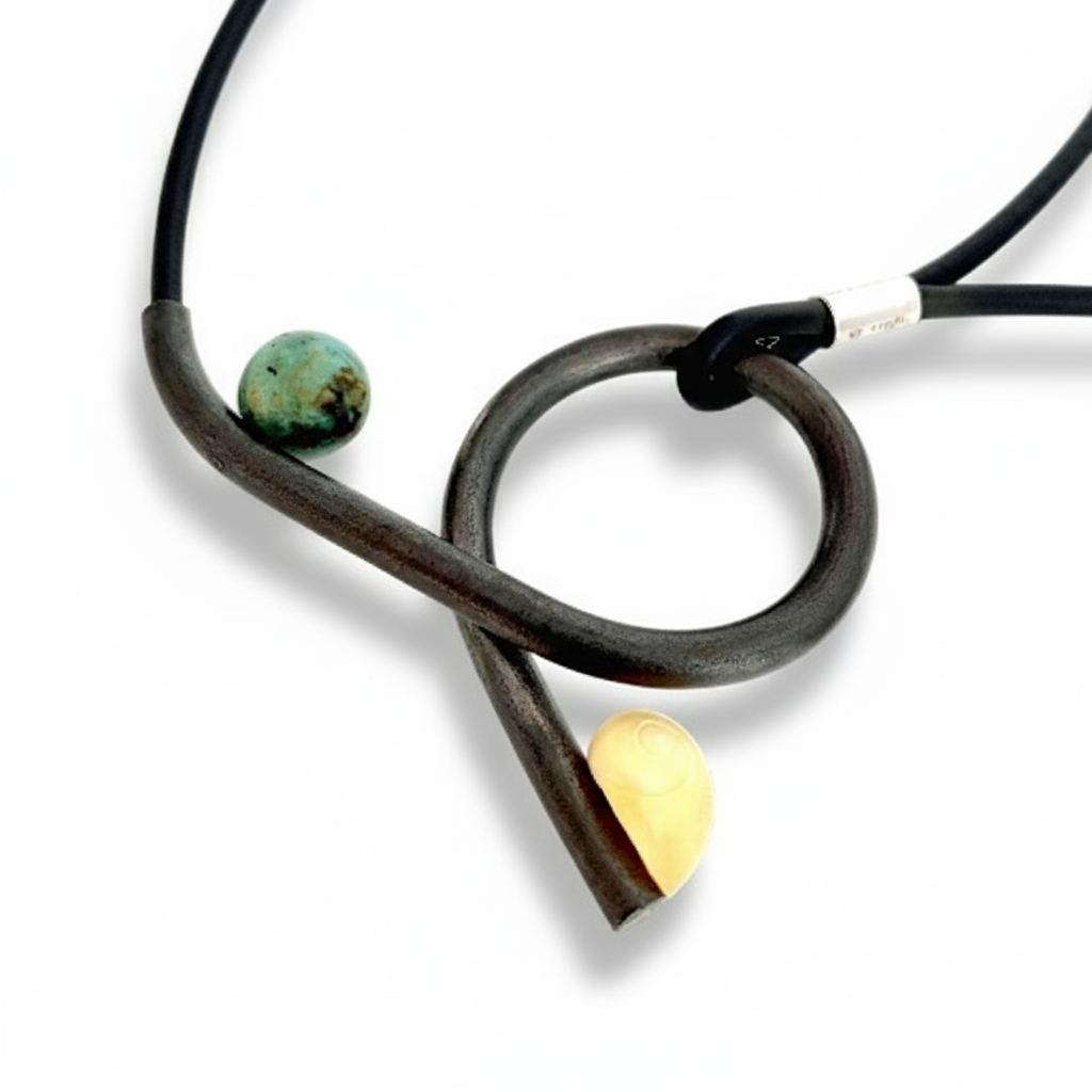 Pendentif en fer forgé paré d'un coquillage jaune et d'une ronde verte presenté sur lien de caoutchouc. Un bijou poétique inspiré par la nature. pièce unique 2017 signée Marianne Anselin, artiste française.