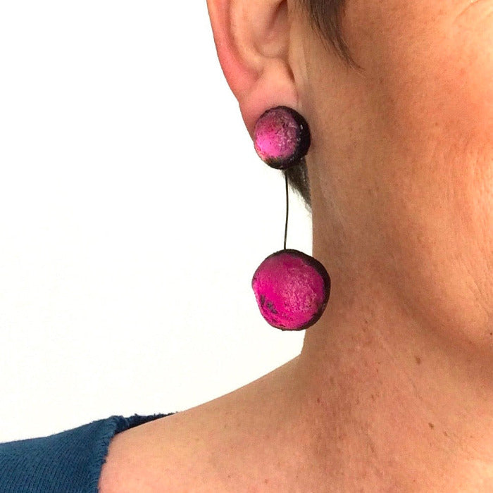 Boucles d'oreilles constituées de 2 sphères en résine irisée fushia, reliées par un cable noir.
