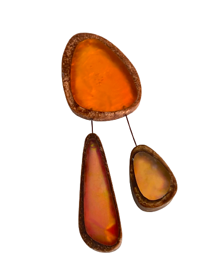 Broche en résine orange composée de trois éléments de différentes tailles,deux petits éléments sont reliés au plus grand par un cable rigide noir. fermeture aimant. broche posée sur fond blanc