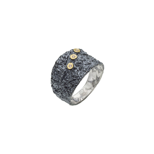 Cette bague en argent patiné et texturé se distingue par trois diamants taille brillant, sertis en or jaune sur dessus, alignés de côté.
