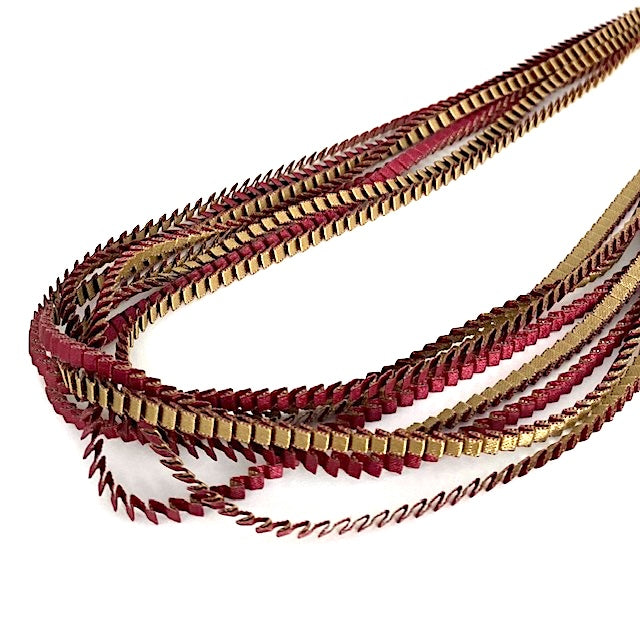 Long sautoir de couleur bordeaux et olive composé de huit bandes de satin plissé reliées les unes aux autres par un lien de coton jaune. Détail sur le plissé du collier.