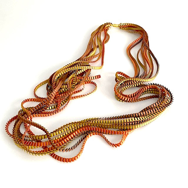 Long sautoir de couleur marron, doré, cuivré composé de huit bandes de trois millimètres de satin plissé reliées les unes aux autres par un lien de coton jaune d'or.