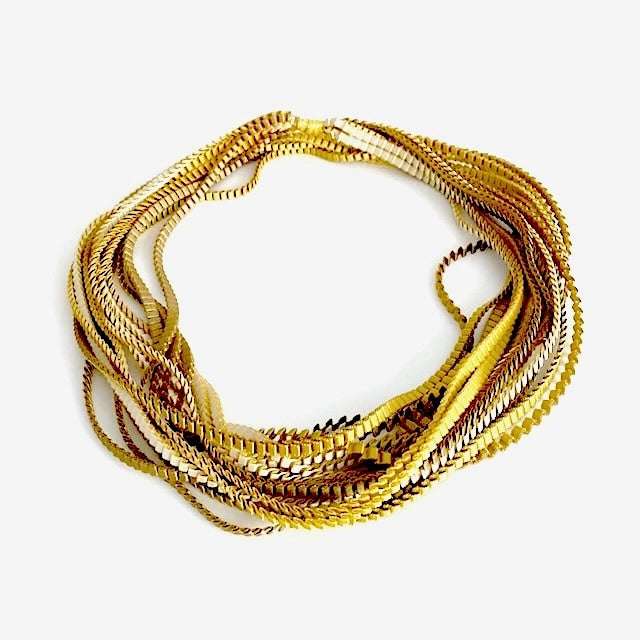 Sautoir de couleur kaki, ivoire et doré composé de huit bandes de trois millimètres de satin plissé reliées les unes aux autres par un lien de coton jaune d'or. Peut être porté long et en double selon vos envies.