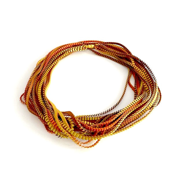 Sautoir de couleur marron, doré, cuivré composé de huit bandes de trois millimètres de satin plissé reliées les unes aux autres par un lien de coton jaune d'or. À porter ong ou en double selon l'humeur.