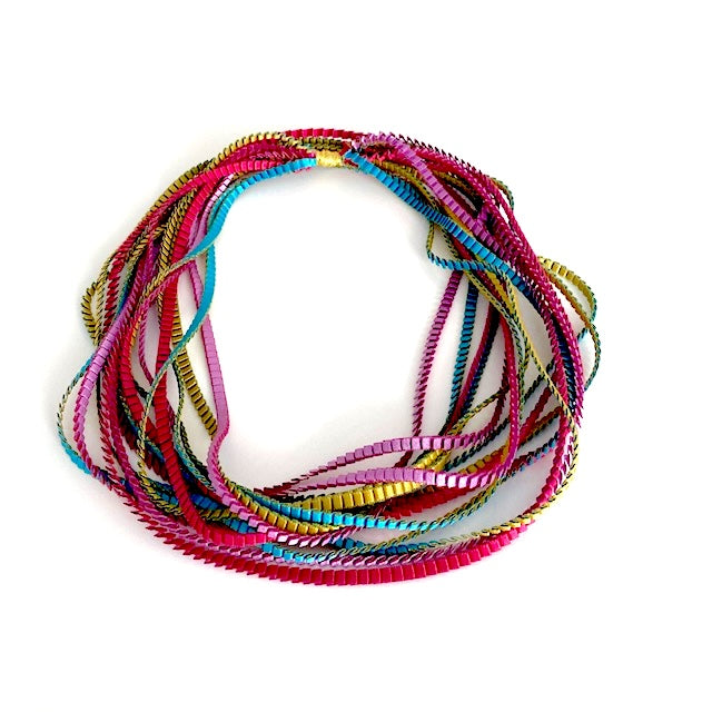 Long sautoir composé de huit bandes de trois millimètres de satin plissé de couleur, doré, turquoise, fuchsia, lilas,reliées les unes aux autres par un lien de coton jaune d'or. 