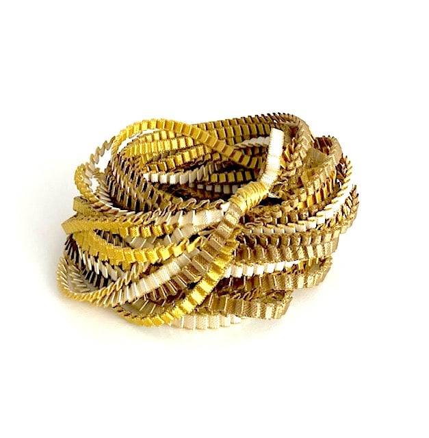 Long sautoir de couleur kaki, ivoire et doré composé de huit bandes de trois millimètres de satin plissé reliées les unes aux autres par un lien de coton jaune d'or.