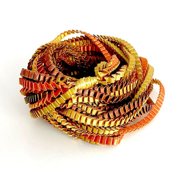 Long sautoir de couleur marron, doré, cuivré composé de huit bandes de trois millimètres de satin plissé reliées les unes aux autres par un lien de coton jaune d'or.