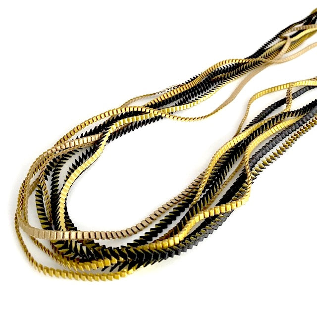  Long sautoir de couleur noir , olive et doré,composé de huit bandes de trois millimètres de satin plissé reliées les unes aux autres par un lien de coton jaune d'or. 