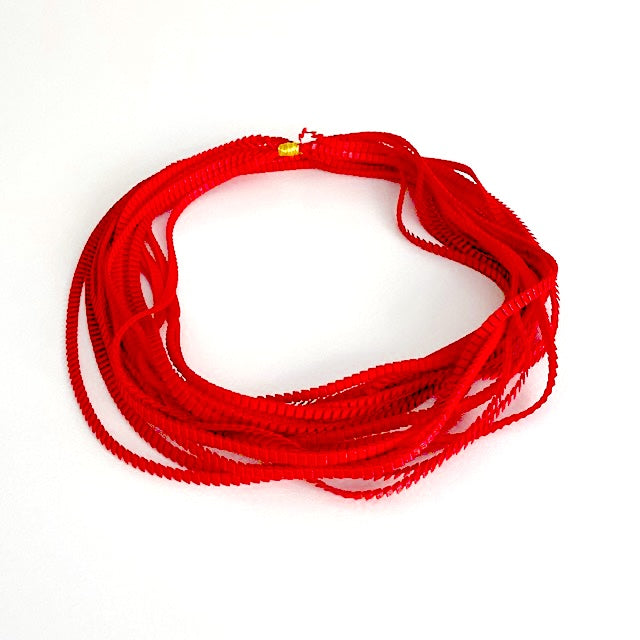 Long sautoir rouge composé de huit bandes de trois millimètres de satin plissé reliées les unes aux autres par un lien de coton jaune d'or.