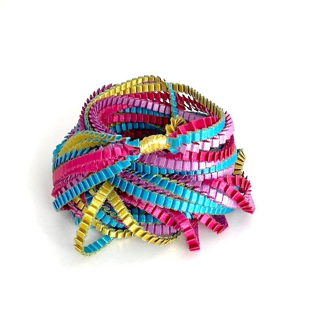 Long sautoir composé de huit bandes de trois millimètres de satin plissé de couleur, turquoise, doré, fuchsia, lilas,reliées les unes aux autres par un lien de coton jaune d'or. 