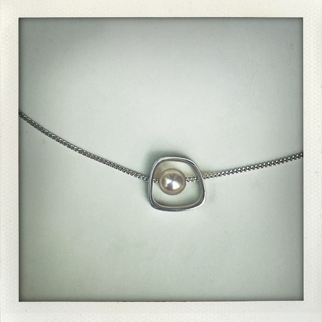 Collier en argent avec pendentif géométrique et perle d’eau douce banche. Fabrication artisanale en argent texturé traversé par une chaîne, création Anne Milbeau.