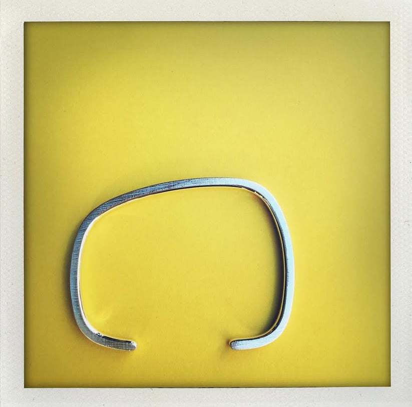 Bracelet géométrique en argent forgé au fil carré, jonc ouvert au design asymétrique. Modèle mixte, surfaces striées et intérieur poli. Bijou design contemporain, bijou minimaliste présenté sur un fond jaune.