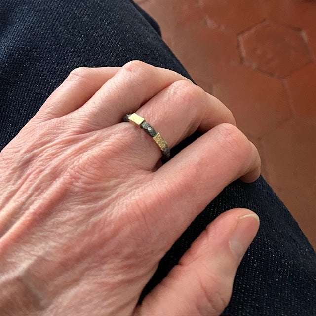 Anneau en argent patiné noir et texturé avec un petit diamant au centre, entre deux rectangles d'or jaune. Bague portée sur le majeur.